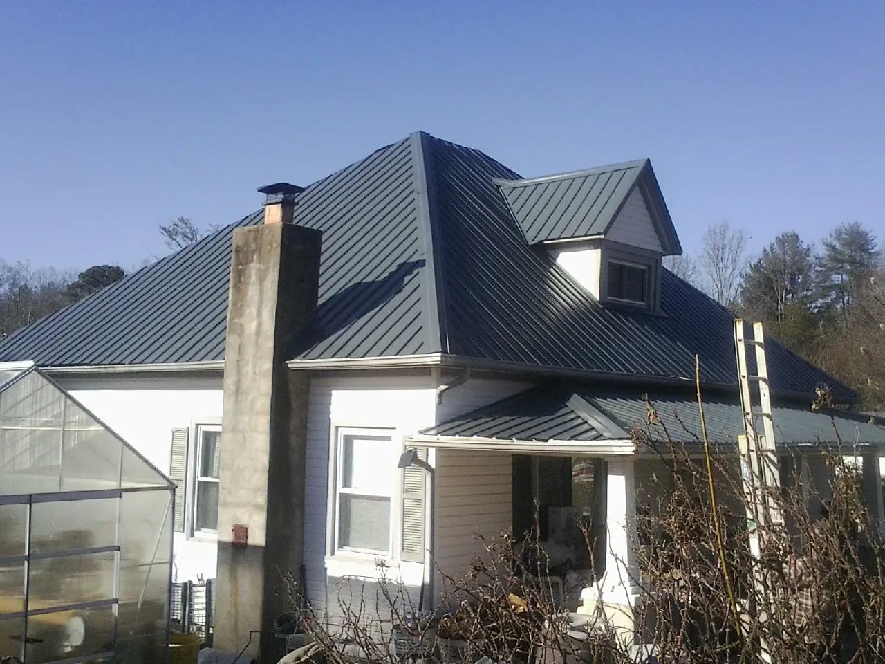 Dark blue standing seam metal roof on a white farmhouse with dormer — Slate & Tile Roof Repair by Roofing Brothers in Grand Canyon