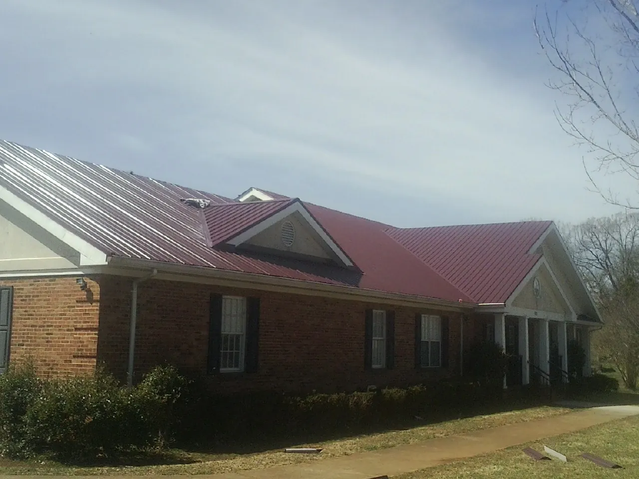 Red metal roof with gabled entries on a long brick building, from a Hail Damage Roof Repair job in Grand Canyon