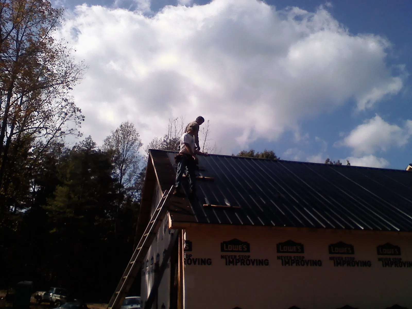 Roofer fastening dark metal panels high against a cloudy sky, from a Roof Inspection job in Grand Canyon